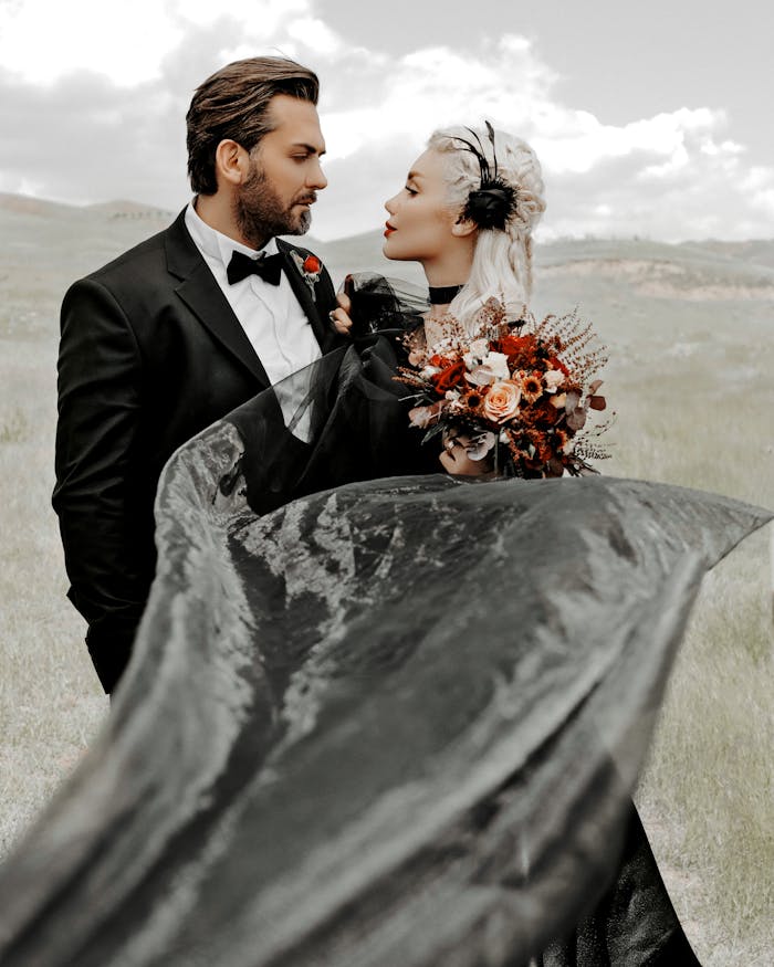 Outdoor wedding photo of a couple in elegant attire with a black gown and bouquet.